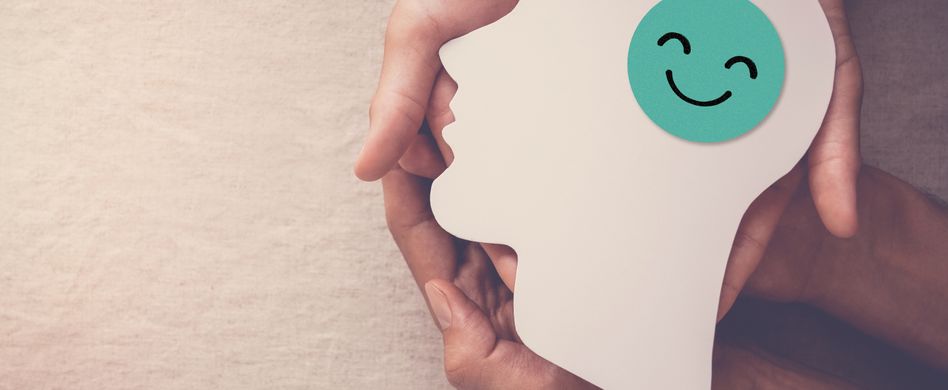 hände halten weißen papierausschnitt in kopfform mit grünem smiley in der mitte auf beigem hintergrund