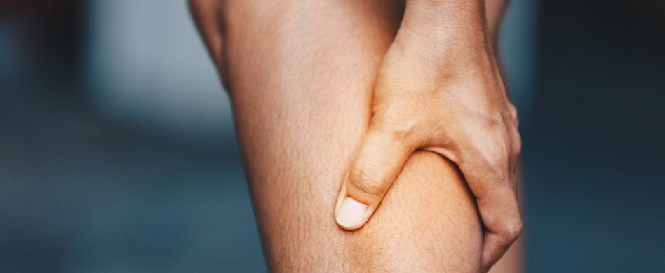 mann hält sich die wade vor dunklem hintergrund