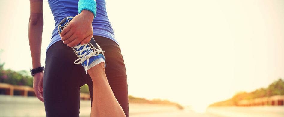 sportlerin wärmt sich vor dem laufen auf straße auf und winkelt ihr rechtes bein nach hinten an