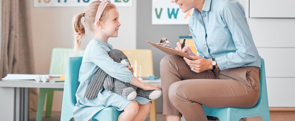 frau sitzt mit kind in raum auf blauen stühlen mit zahlen und buchstaben an der wand im hintergrund