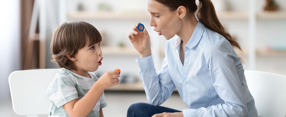 frau sitzt mit kind an tisch und übt mit buchstaben sprechen