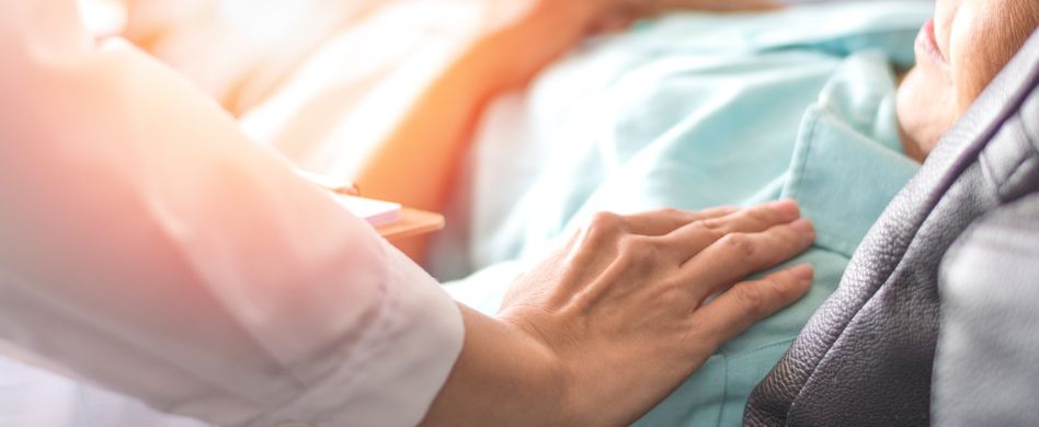 pflegerin hält hand auf kranke person die im bett liegt