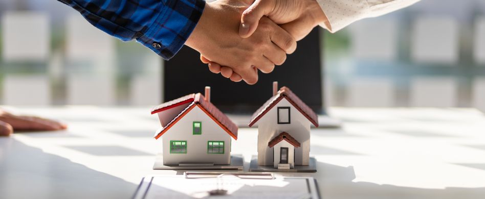 zwei leute geben sich die hand über einem modell mit zwei häusern