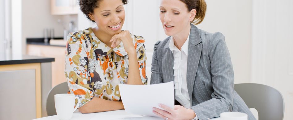 zwei frauen schauen gemeinsam auf ein blatt papier am tisch sitzend