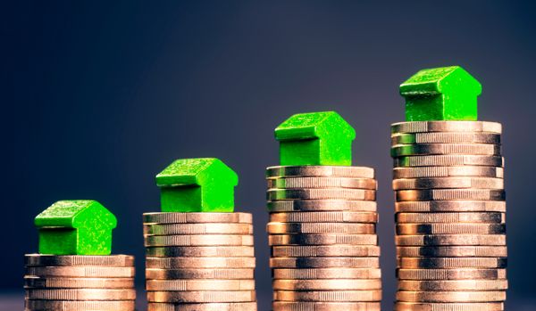 4 münzstapel mit grünen häusern obendrauf