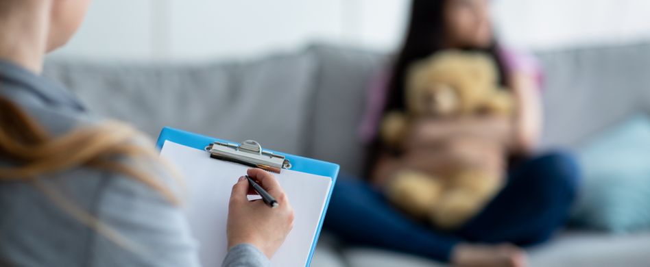 kind sitzt bei therapeutin mit klemmbrett auf sofa