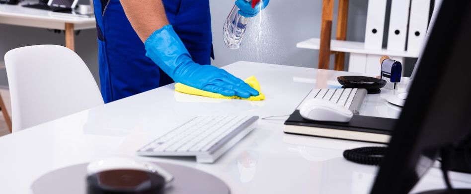 mann reinigt bürotisch mit handschuhen und putzmittel