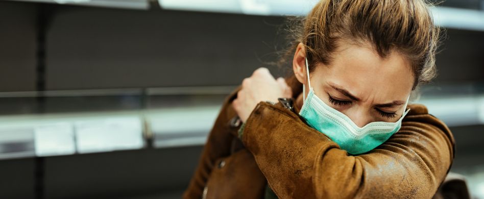 frau mit maske hustet in den ellenbogen