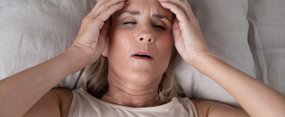Frau im Bett fasst sich an Kopf