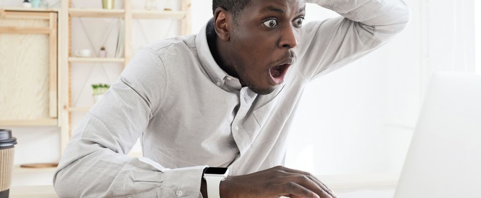 mann schaut erschrocken auf laptop