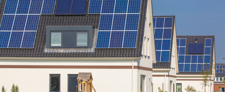 haus mit blauer solaranlage auf dem dach und grünem garten im vordergrund