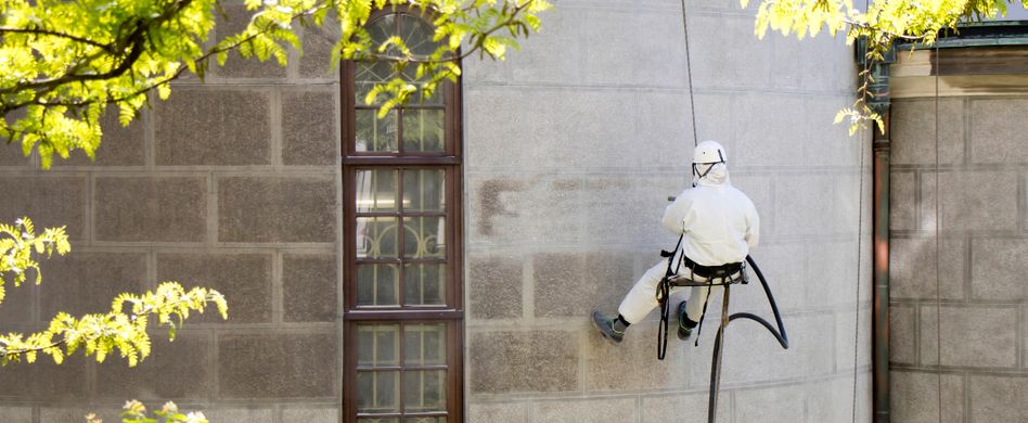 arbeiter mit weißem anzug reinigt fassade
