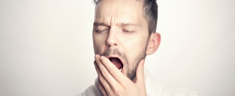gähnender mann hält sich hand vor den mund