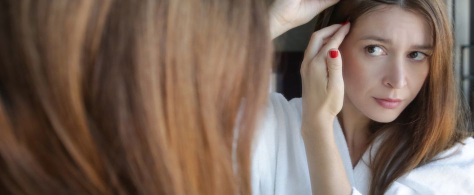 frau schaut sich haare im spiegel an
