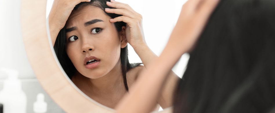 frau schaut sich haare im spiegel an