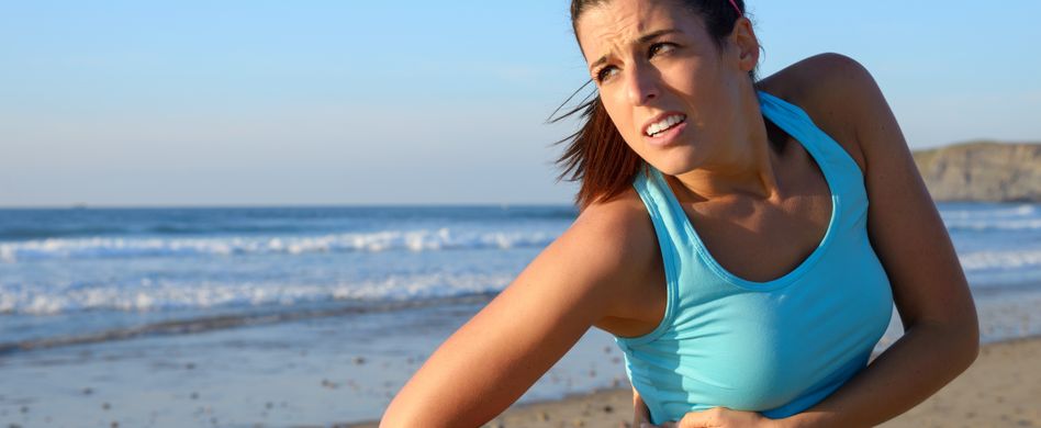 frau mit seitenstechen am strand hält sich die seite