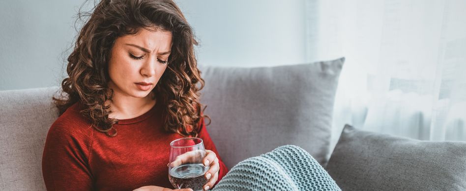 Frau nimmt Medikament mit Wasser auf Sofa