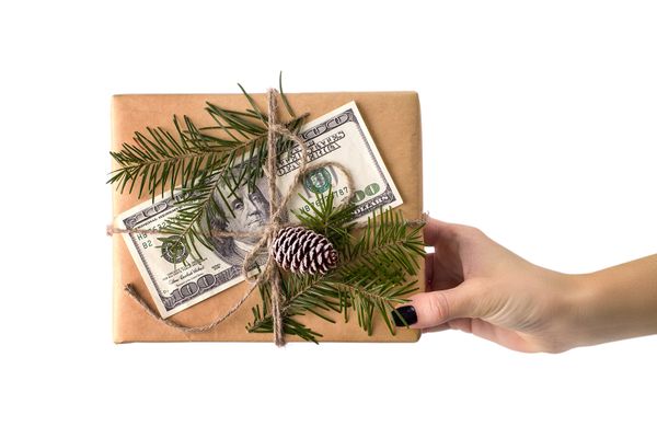 frau hält weihnachtsgeschenk mit geld und papier verpackt mit tannenzweigen