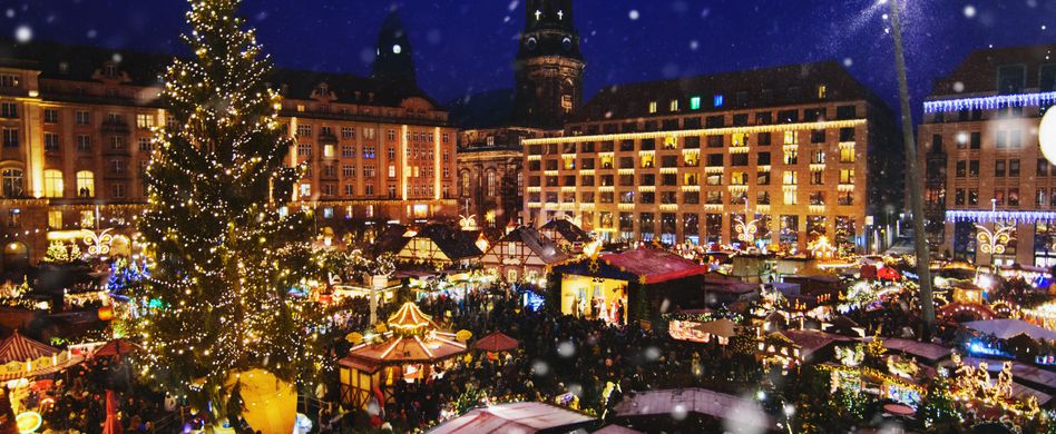 weihnachtsmarkt mit vielen bunten loichtern weihnachtsbaum und schnee vor häuserreihe und blauem nachthimmel