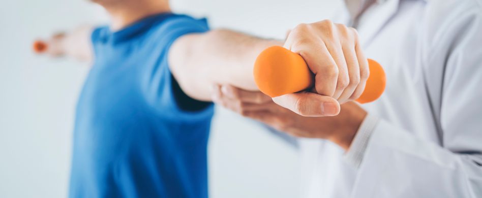 physiotherapeut gibt mann in blauem shirt behandlung mit orangenen hanteln