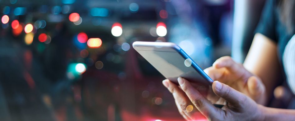 person hält smartphone in der hand bei nacht und bunten lichtern im hintergrund