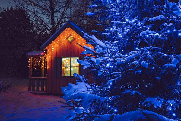weihnachtsbeleuchtung am gartenhaus hinter tannenbaum mit schnee