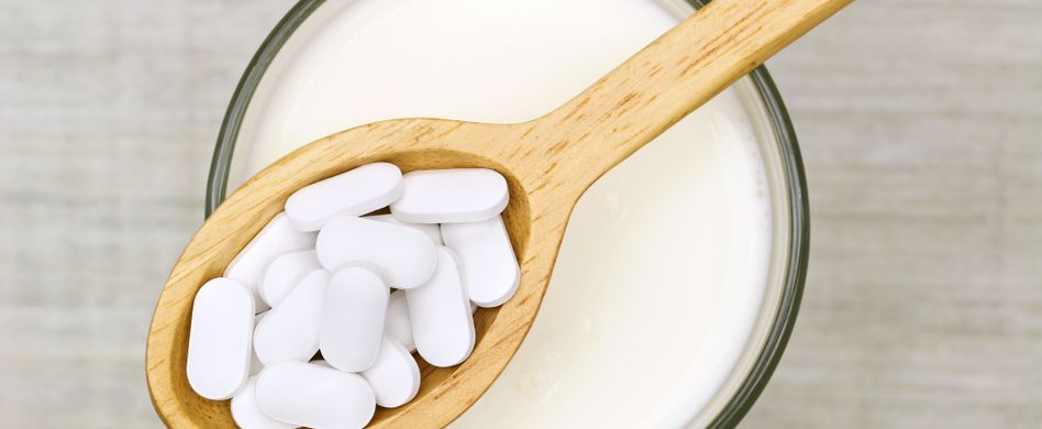 calcium tabletten auf holzlöffel über milchglas